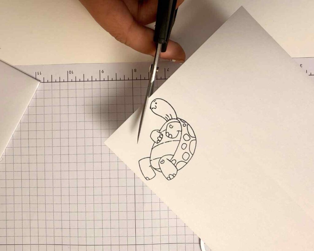 A stamped turtle image is carefully trimmed from masking paper to prepare for layered stamping on a handmade card.