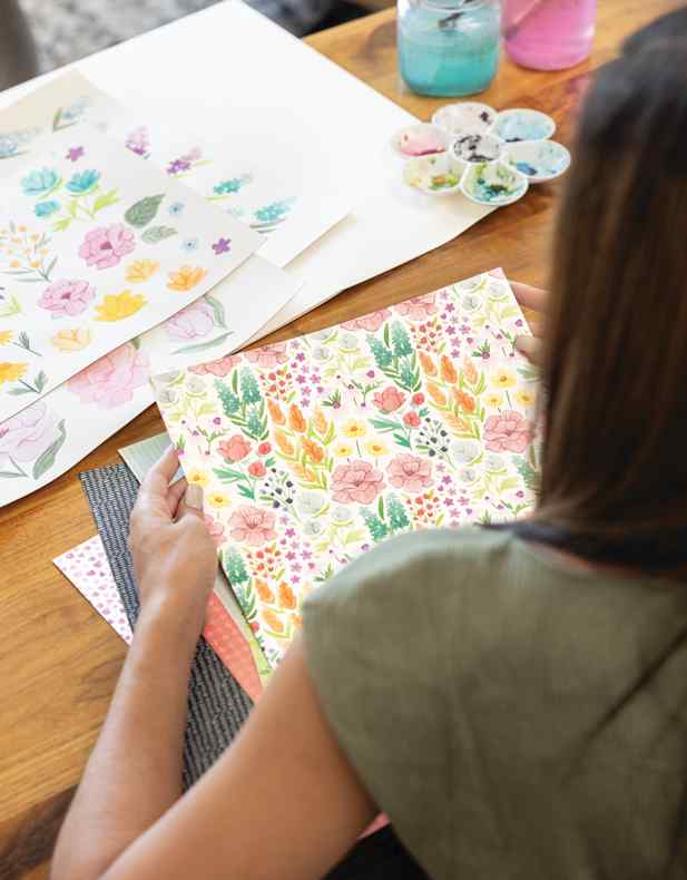 Creatieveling sorteert scrapbookpapier met patronen aan een bureau met verf en materiaal in de buurt, ter illustratie van het opruimen en organiseren van scrapbookingmateriaal.