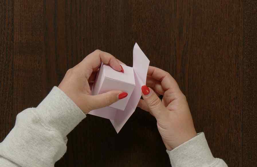 Folding the top flap into place to create the finished lid of a handmade paper gift box.