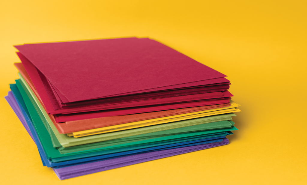 Stack of colorful cardstock sheets arranged in rainbow order on a bright yellow background.