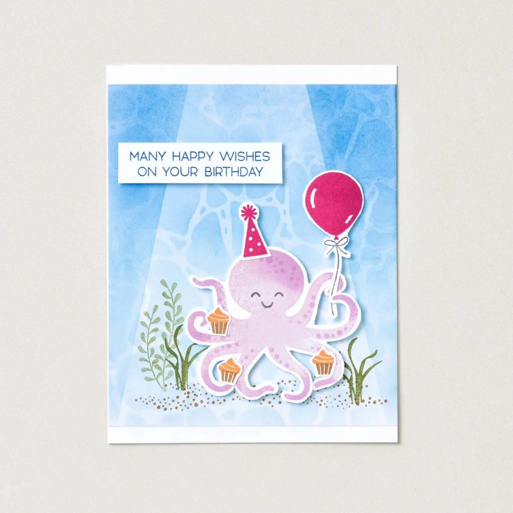 Cute underwater DIY birthday card featuring a smiling octopus wearing a party hat, holding a balloon, with birthday cupcakes and ocean plants.