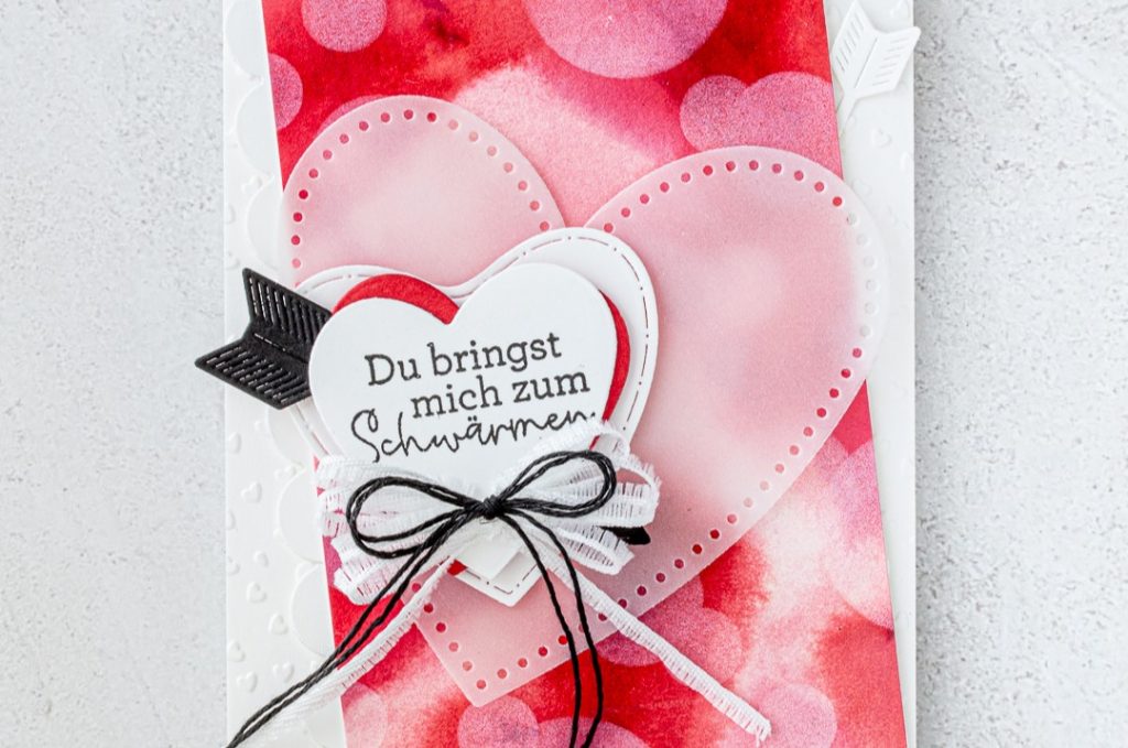 Carte faite main présentant un fond « bokeh » rose et rouge, agrémentée de cœurs découpés superposés, de rubans décoratifs et d'un message plein de tendresse.