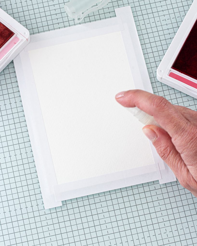 Le papier aquarelle est fixé à l'aide de papier de masquage, tandis qu'un vaporisateur d'eau est utilisé pour préparer la surface en vue de réaliser facilement un arrière-plan avec effet bokeh.