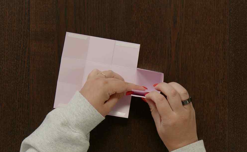 Pressing the adhesive into place while assembling the sides of a handmade cardstock gift box.