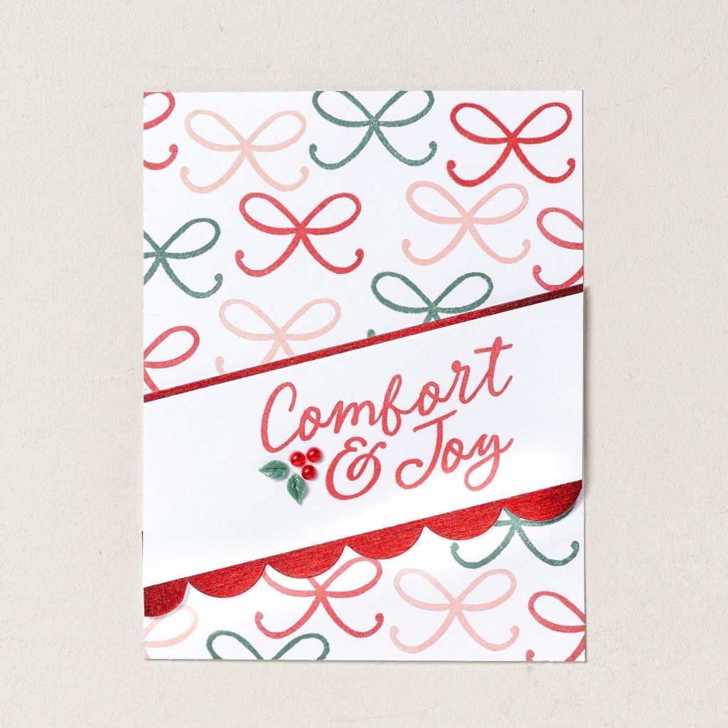 Witte kerstkaart met rode, roze en groene gestempelde strikken, een 'Comfort & Joy'-wens en een rode geschulpte rand.