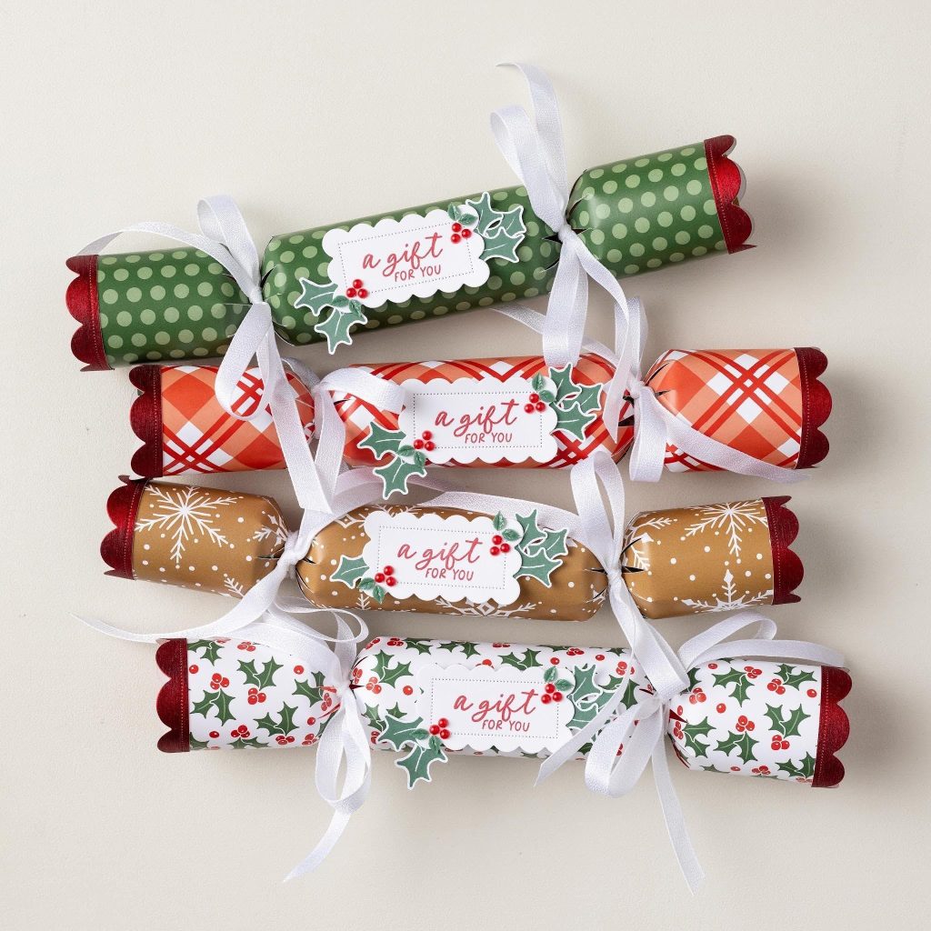Vier papieren kerstcrackers met feestelijke patronen, witte linten, hulstaccenten en labels met de tekst 'a gift for you'.