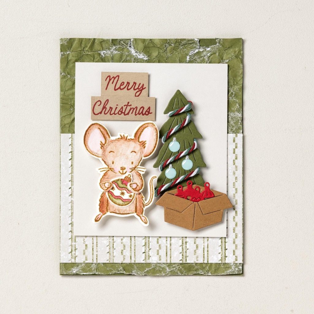 Carte de Noël représentant une souris tenant une boule de Noël, un sapin décoré, une boîte à boules de Noël et le message « Joyeux Noël » sur du papier vert vieilli.