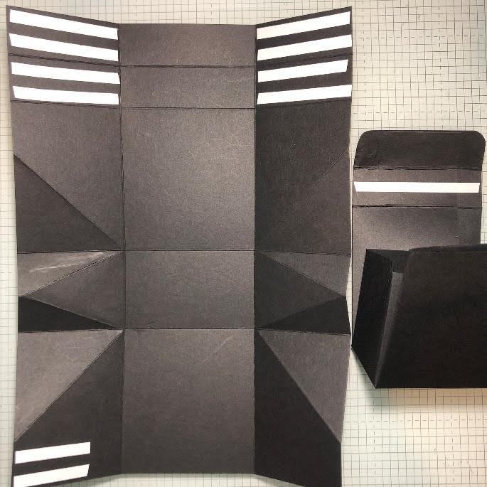 Black cardstock gift bag template with folded triangular sides, adhesive strips, and a partially assembled paper bag