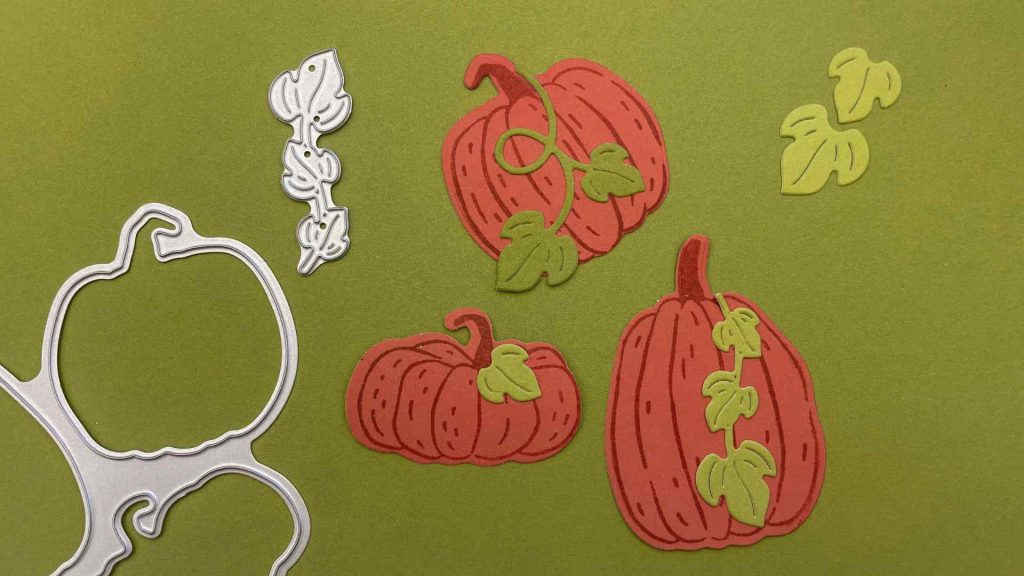 Des citrouilles en papier orange réalisées à la main, ornées de feuilles vertes découpées à l'aide de poinçons et de motifs métalliques, sur un fond vert olive