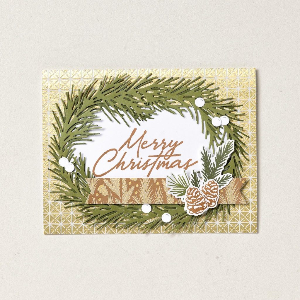 Une couronne verte à feuilles persistantes entoure les lettres « Joyeux Noël » sur papier doré à motifs, accentuées de pommes de pin et de points blancs.
