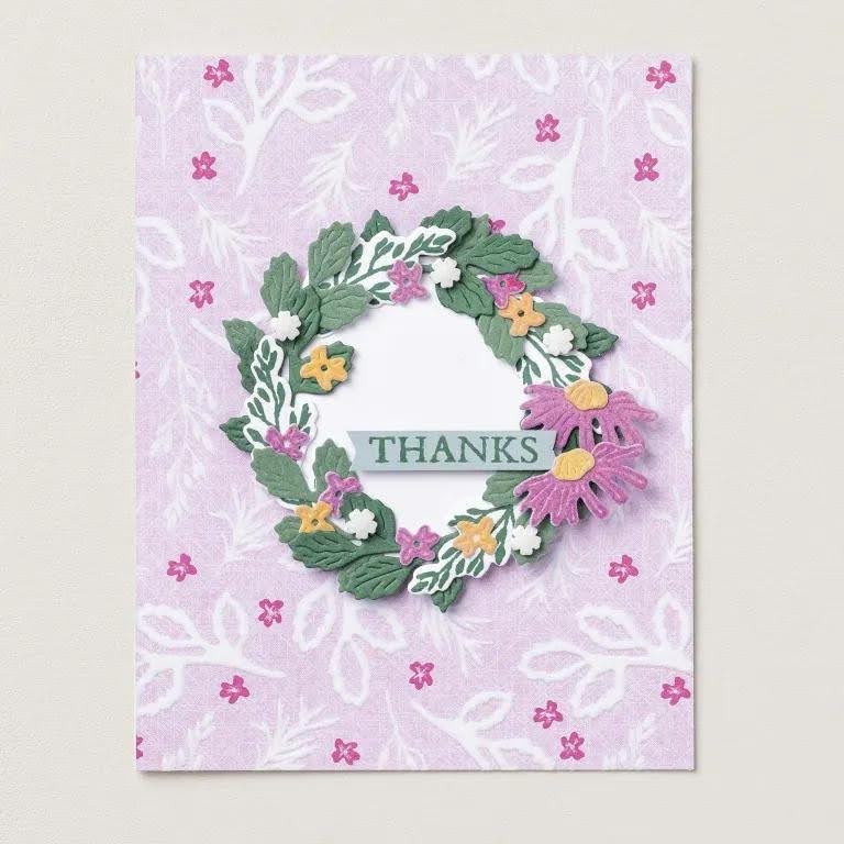 Une carte à motifs roses est ornée d'une couronne de feuilles vertes, de fleurs roses et jaunes, ainsi que d'une banderole verte portant l'inscription « THANKS ».