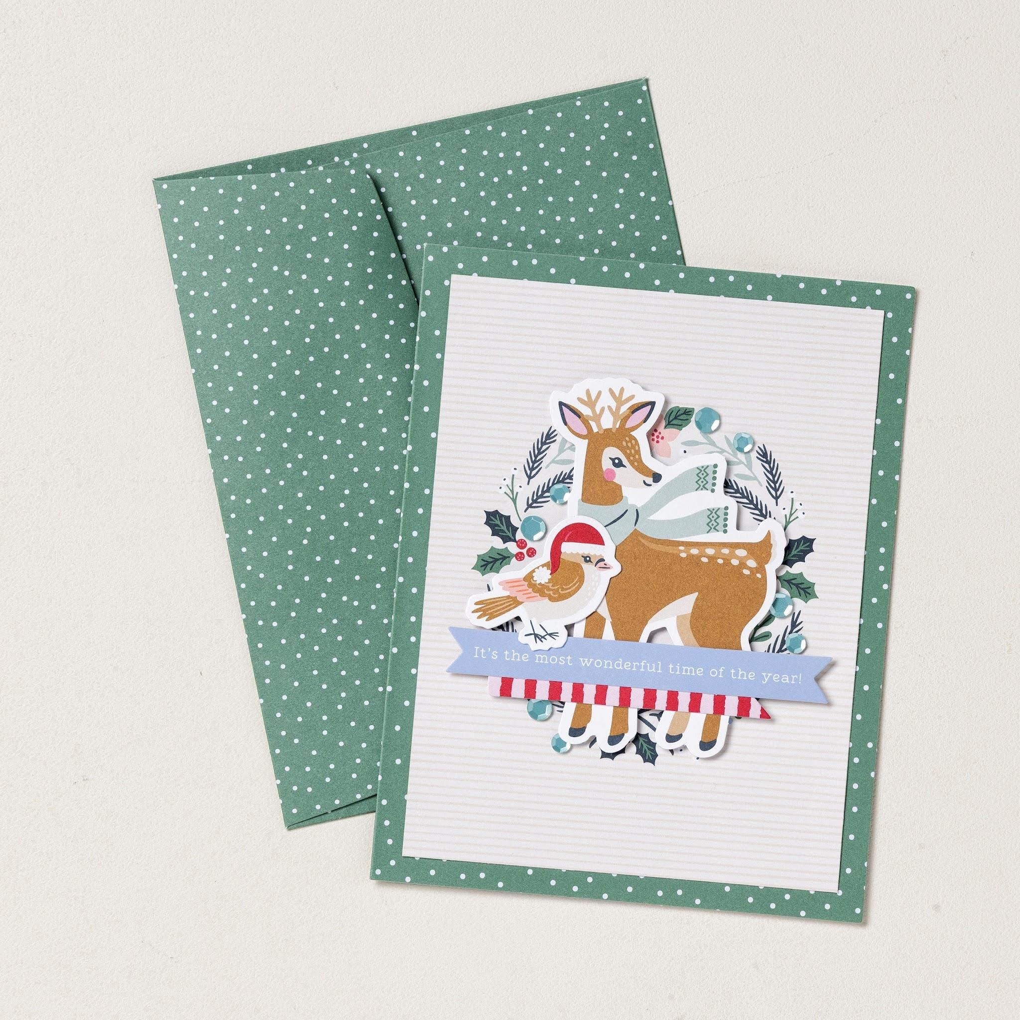 Carte de Noël faite main représentant un renne, un oiseau, des feuillages d'hiver, avec des touches de bleu, accompagnée d'une enveloppe verte à pois assortie.