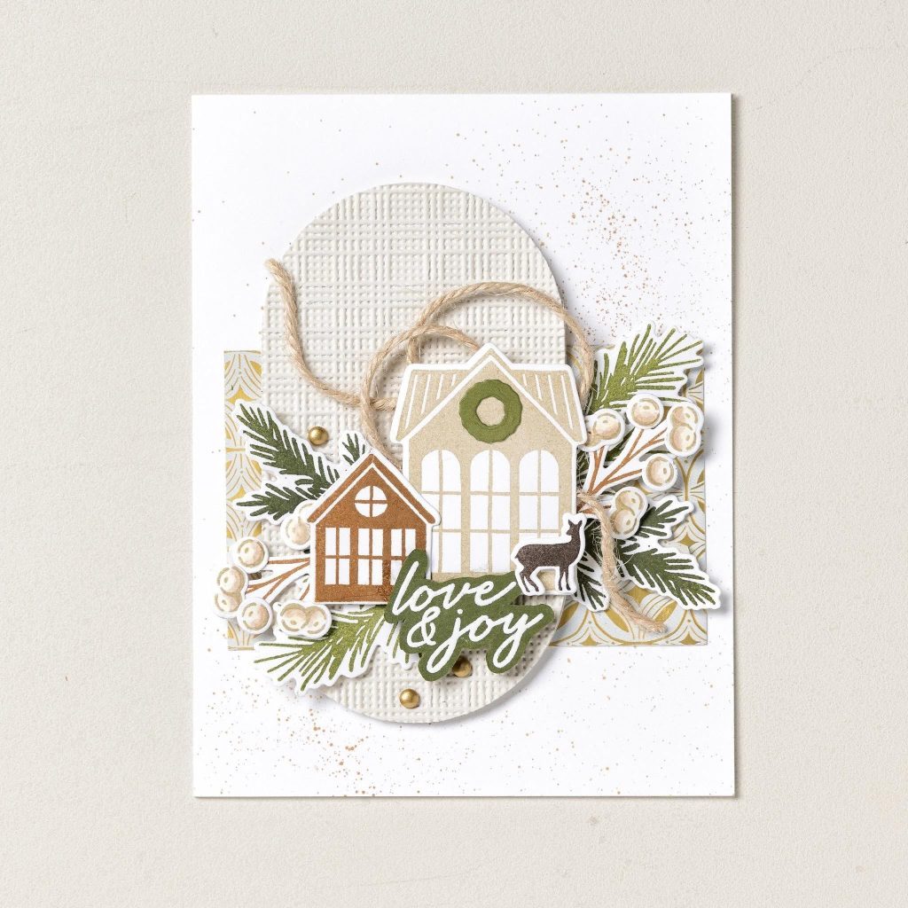 Carte de Noël blanche représentant deux maisons, des brins de conifères, un cerf, de la ficelle et une inscription « love & joy » sur un ovale en relief.